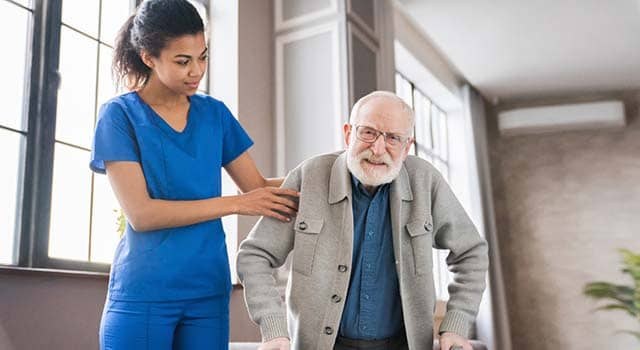 A home health aide assisting an older man as he walks at home